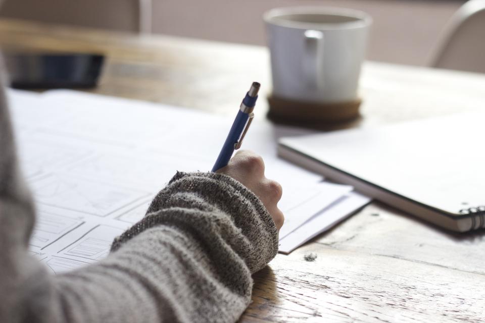 Hands writing in a notebook beside a cup of coffee — spending energy on what you are building